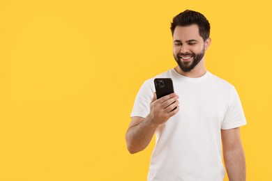 Photo of Happy young man using smartphone on yellow background, space for text