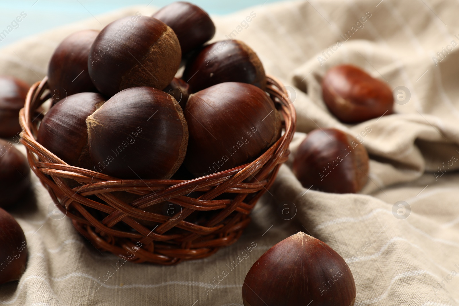 Photo of Wicker bowl with roasted edible sweet chestnuts on table, closeup