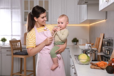 Photo of Happy young woman and her cute little baby spending time together in kitchen