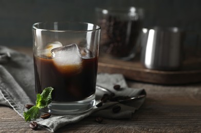Glass of delicious iced coffee, mint and beans on wooden table, space for text