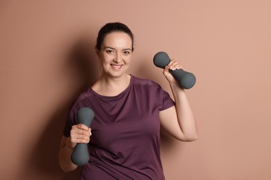 Photo of Happy overweight woman doing exercise with dumbbells on pale pink background