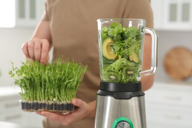 Man holding microgreen peas for delicious smoothie and blender with ingredients in kitchen, closeup