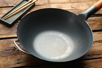 Photo of Empty iron wok and chopsticks on wooden table, closeup