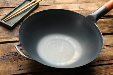 Empty iron wok and chopsticks on wooden table, closeup