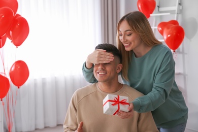 Woman presenting gift to her boyfriend in room decorated with heart shaped balloons. Valentine's day celebration