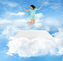 Image of Young woman jumping on mattress in clouds