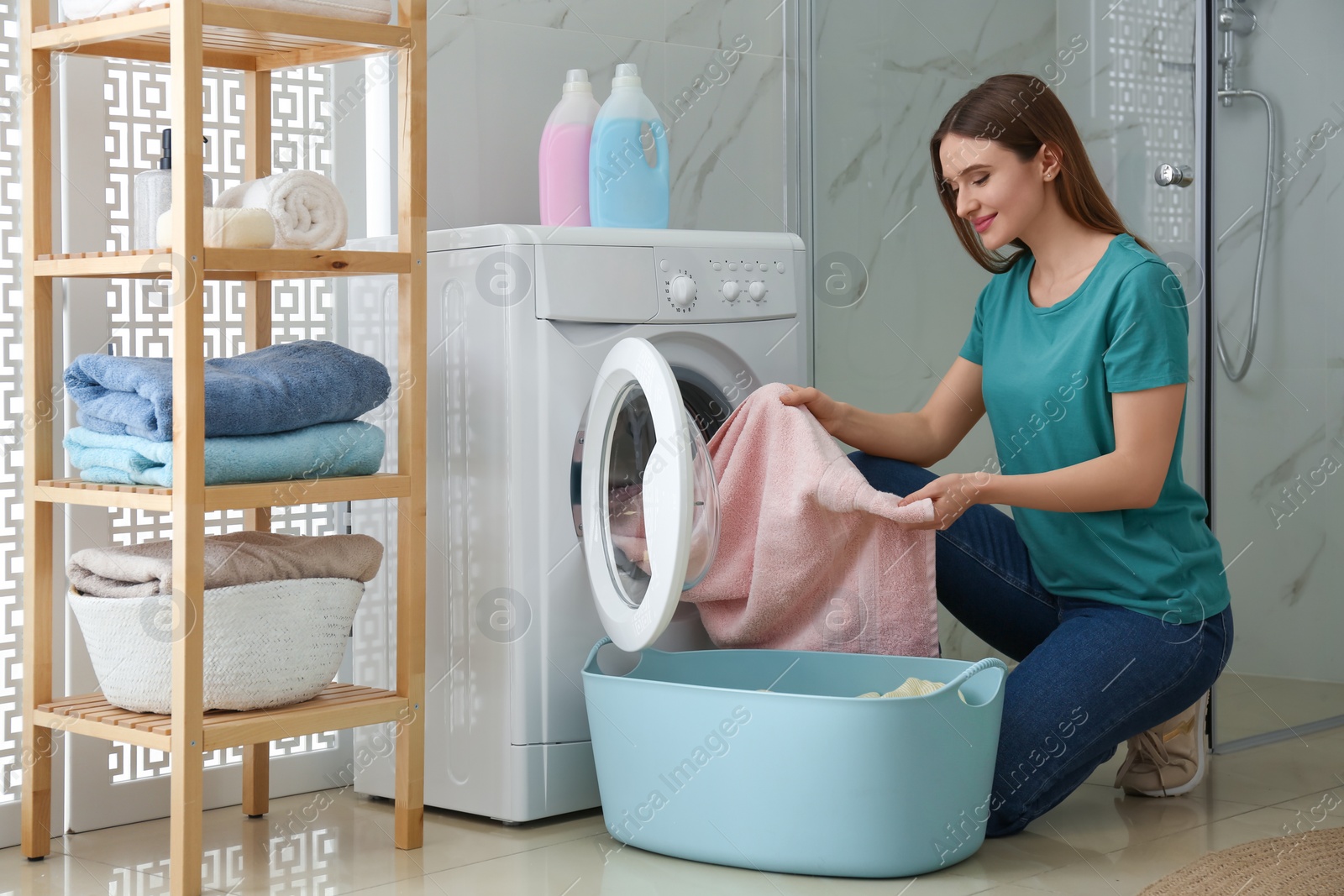 Photo of Young woman with clothes near washing machine in bathroom. Laundry day