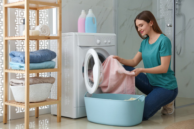 Young woman with clothes near washing machine in bathroom. Laundry day