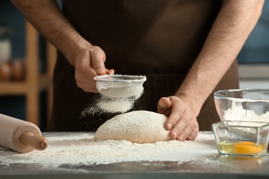 Photo of Man sprinkling flour over dough on table in kitchen