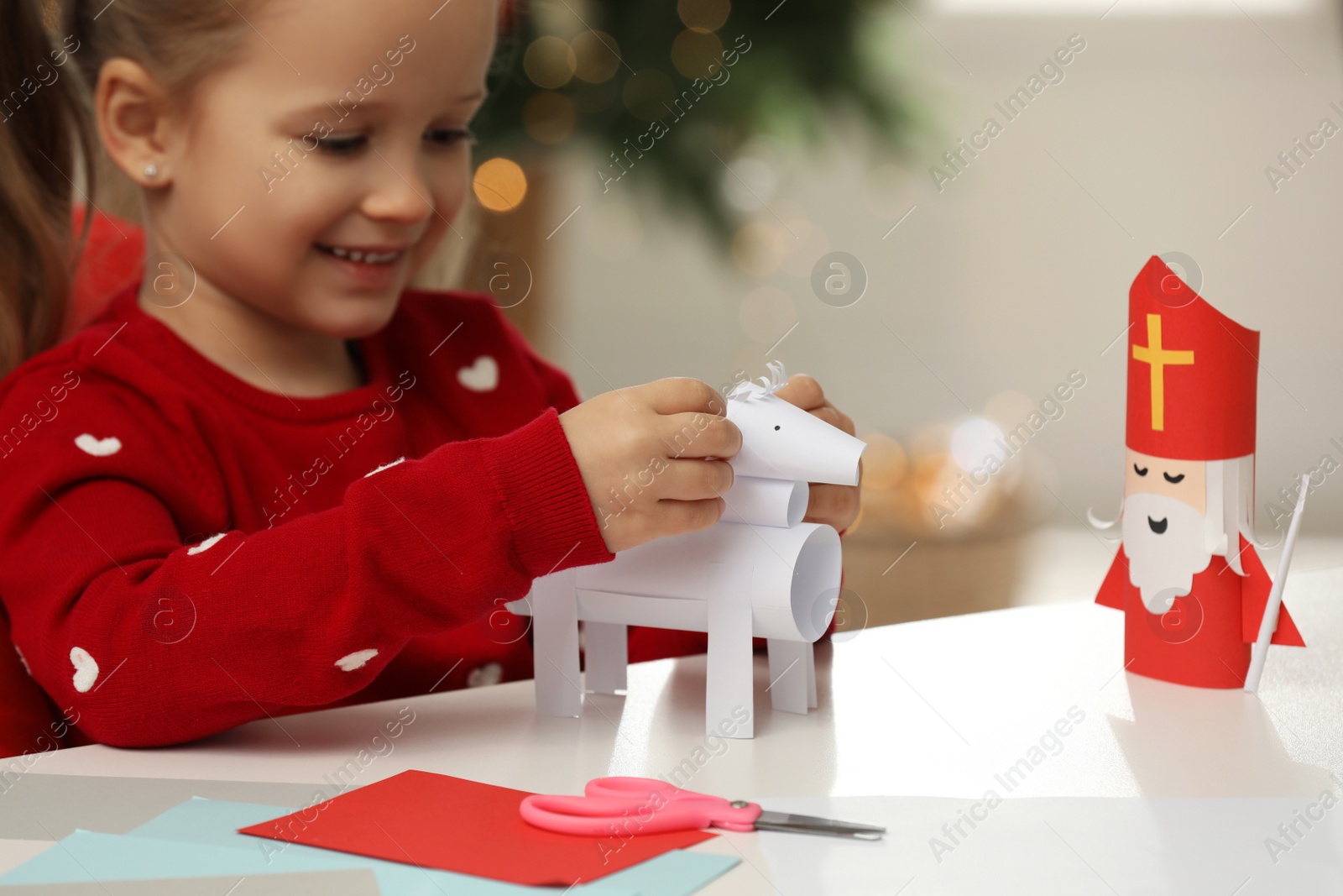 Photo of Cute little girl making paper toy for Saint Nicholas day at home, focus on hand