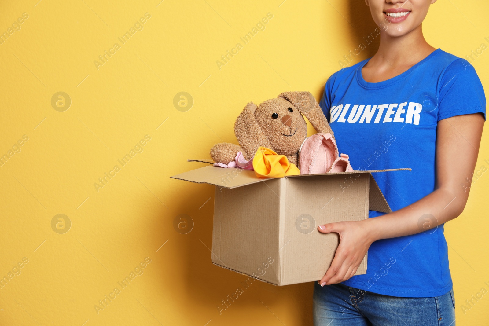 Photo of Female volunteer holding box with donations on color background. Space for text