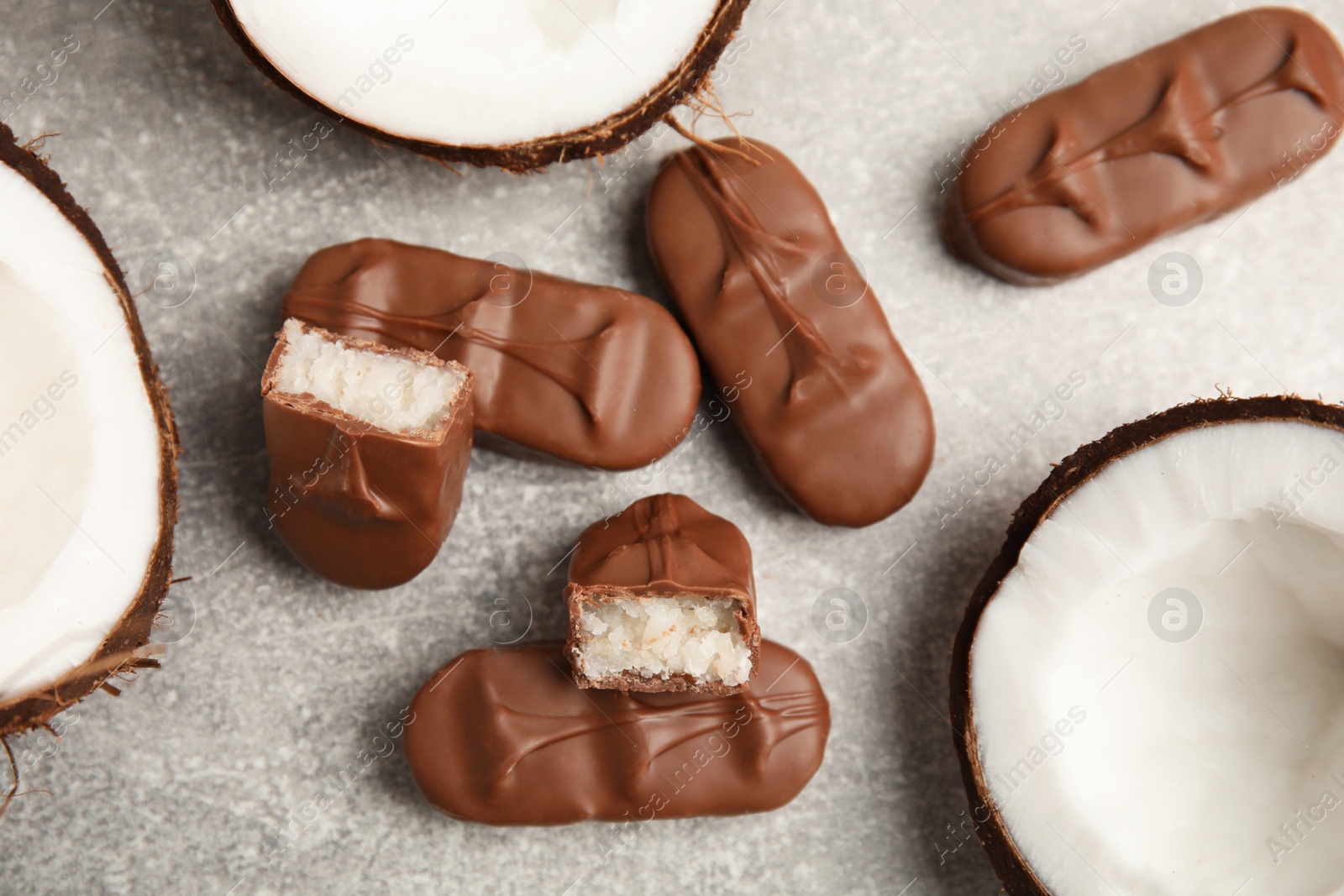 Photo of Delicious milk chocolate candy bars with coconut filling on grey table, flat lay