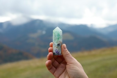 Photo of Woman holding beautiful crystal in mountains, closeup