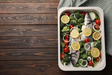 Raw fish with vegetables and lemon in baking dish on wooden table, top view. Space for text