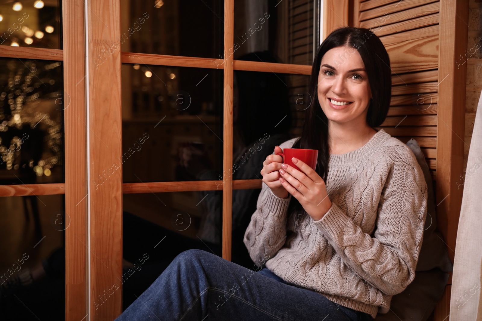 Photo of Beautiful woman with cup of coffee near window indoors. Christmas celebration