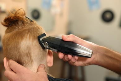 Photo of Professional hairdresser cutting boy's hair in beauty salon, closeup