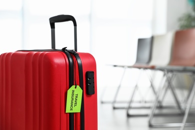 Red suitcase with TRAVEL INSURANCE label indoors, closeup. Space for text