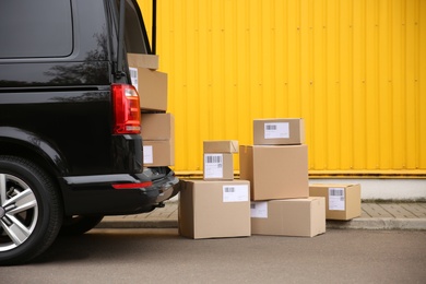 Photo of Black delivery van and many different parcels near yellow building outdoors. Courier service