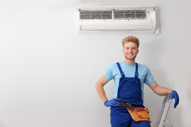 Professional technician near modern air conditioner indoors