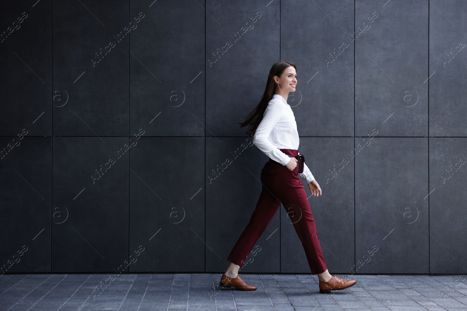 Photo of Young woman in formal clothes walking near grey wall outdoors, space for text