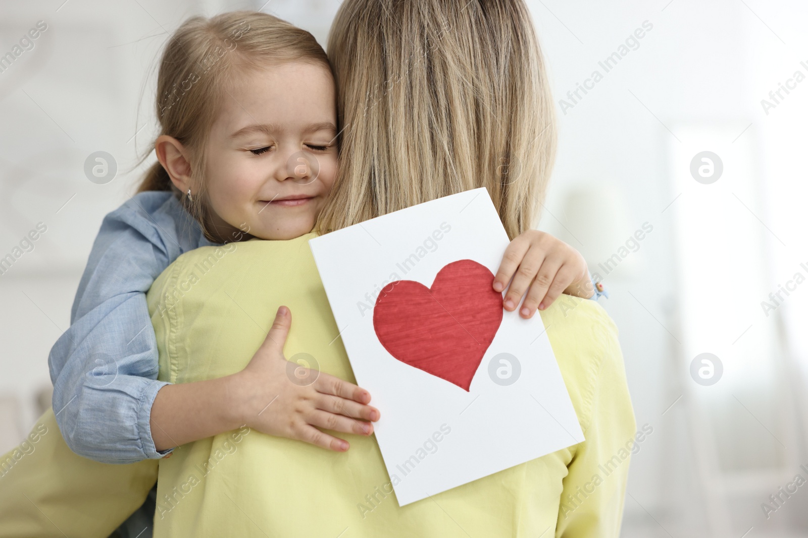 Photo of Little daughter congratulating her mom with greeting card at home. Happy Mother's Day