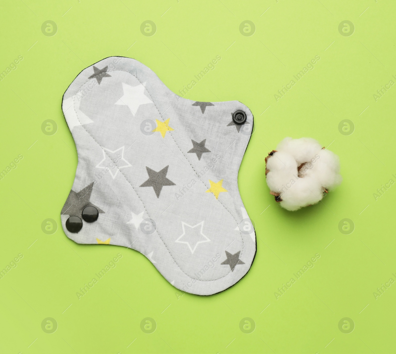 Photo of Reusable cloth menstrual pad and cotton flower on green background, flat lay
