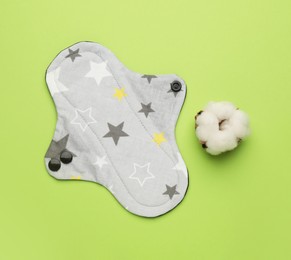 Reusable cloth menstrual pad and cotton flower on green background, flat lay