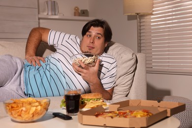 Photo of Overweight man with bowl of popcorn on sofa at home