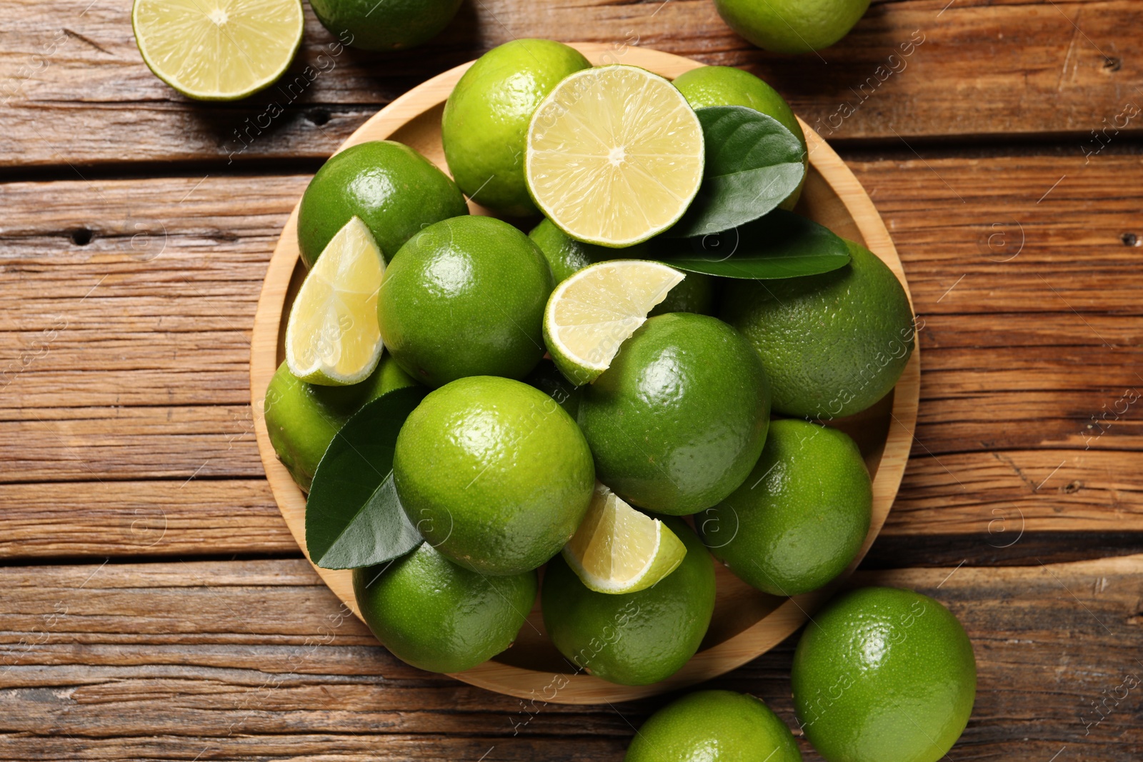 Photo of Fresh limes and green leaves on wooden table, top view