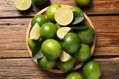 Fresh limes and green leaves on wooden table, top view