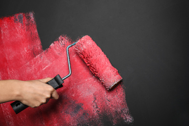 Photo of Woman painting grey wall with pink dye, closeup