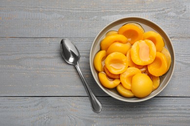 Photo of Canned peach halves and spoon on grey wooden table, flat lay. Space for text
