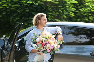Photo of Young handsome man with beautiful flower bouquet near car on street