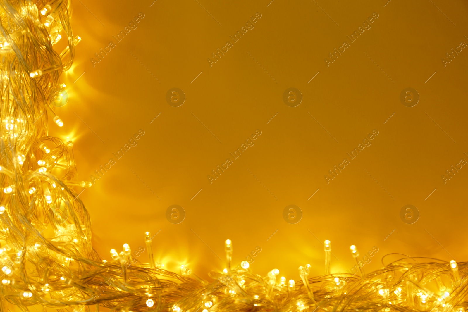 Photo of Glowing Christmas lights on yellow background, top view. Space for text