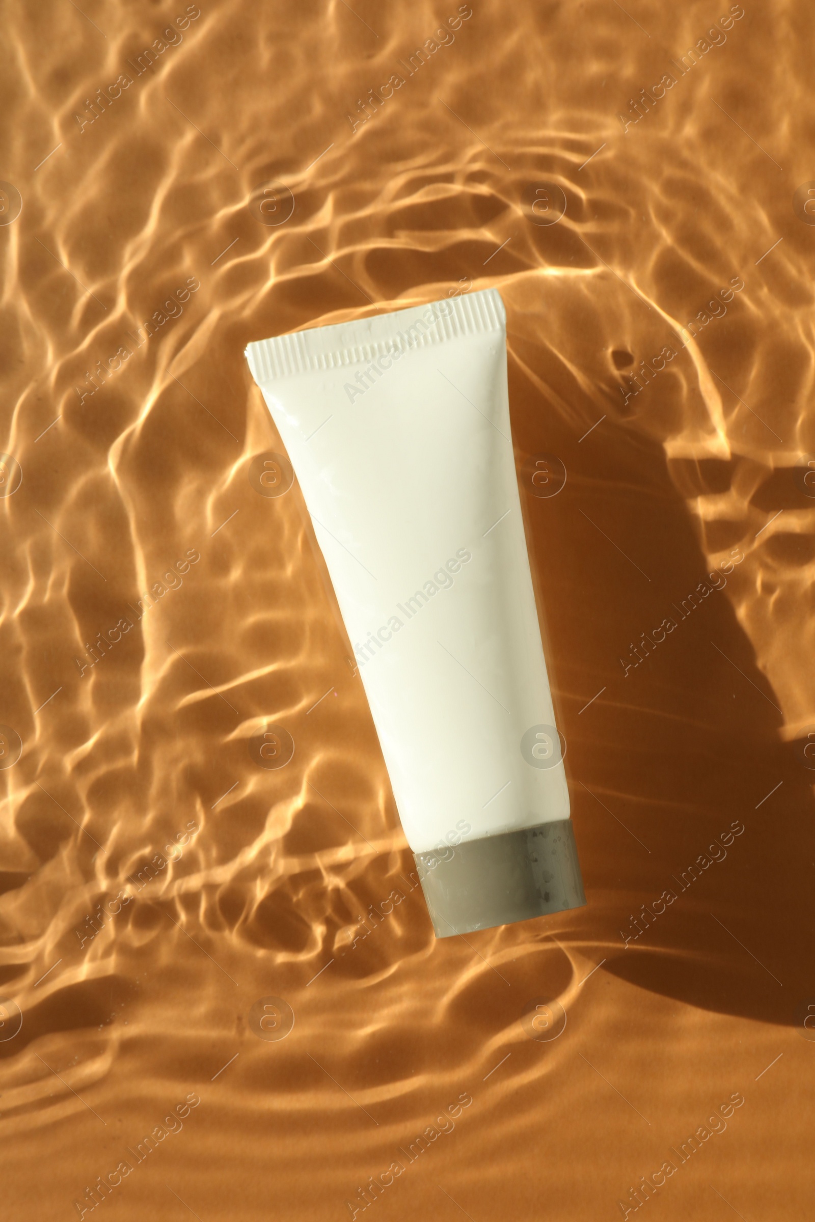 Photo of Tube with moisturizing cream in water on orange background, top view