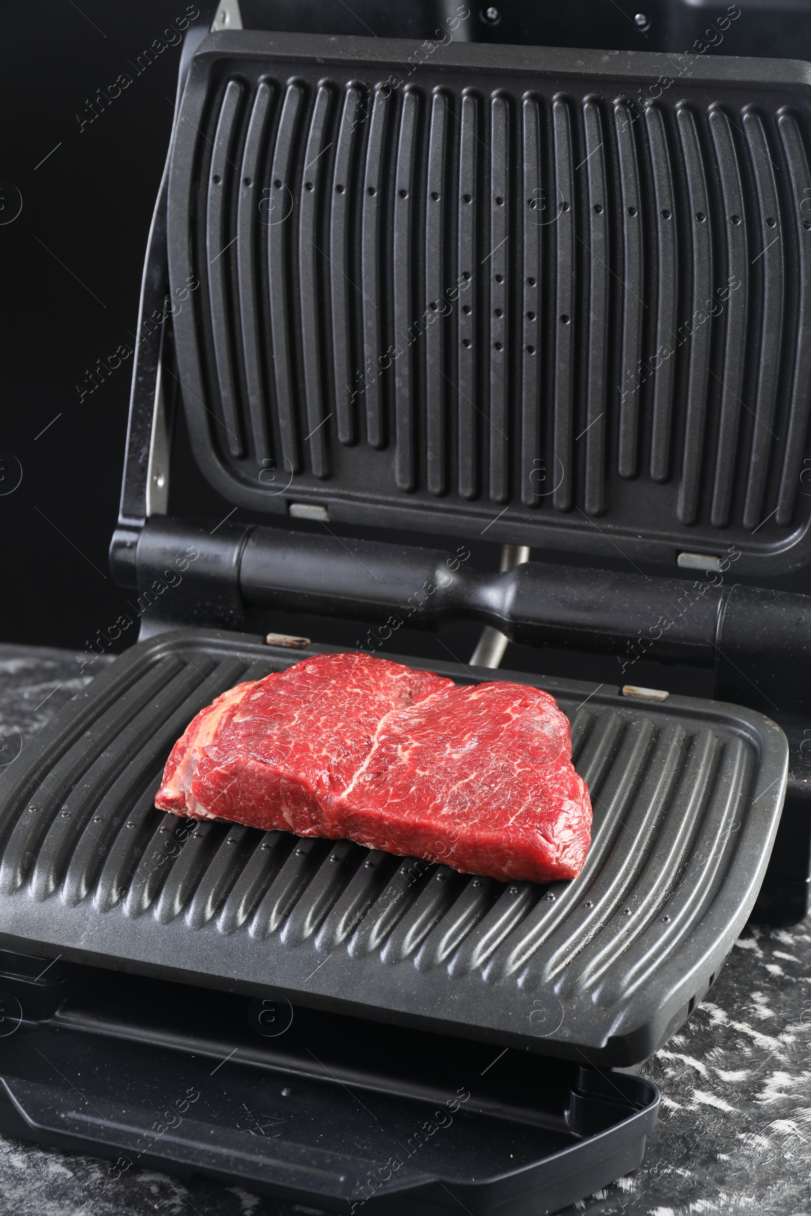 Photo of Cooking fresh beef cut on electric grill at black table