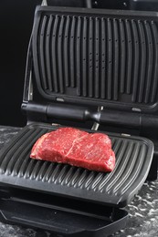 Photo of Cooking fresh beef cut on electric grill at black table