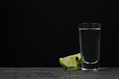 Photo of Shot of vodka with lime slice and mint on grey table. Space for text