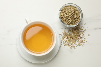 Photo of Fennel tea in cup and seeds on white marble table, flat lay