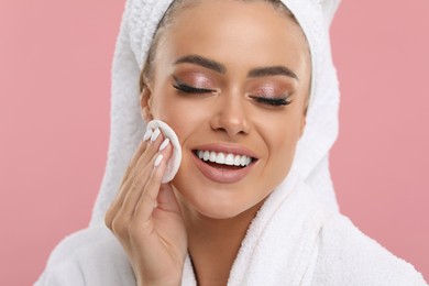 Beautiful woman removing makeup with cotton pad on pink background