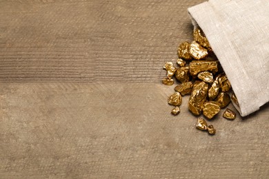 Photo of Overturned sack of gold nuggets on wooden table, flat lay. Space for text
