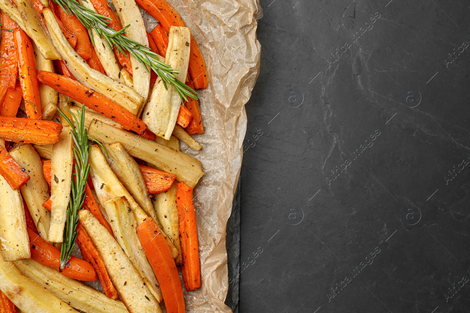 Photo of Parchment with tasty baked parsnip and bell pepper on dark grey table, top view. Space for text