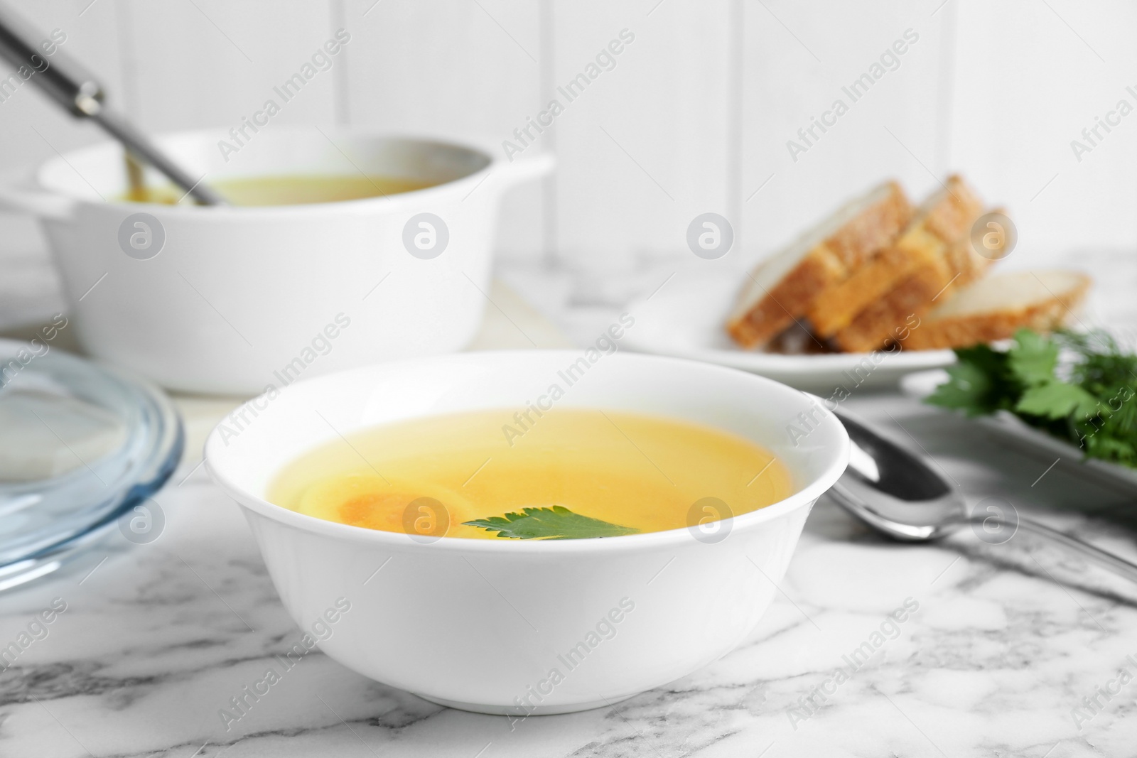 Photo of Delicious bouillon with egg and parsley in bowl on white marble table