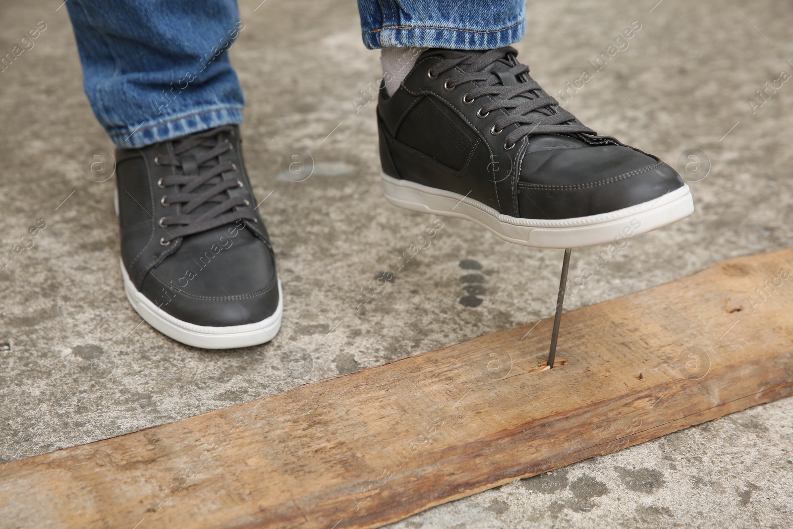 Photo of Careless man stepping on nail in wooden plank outdoors, closeup