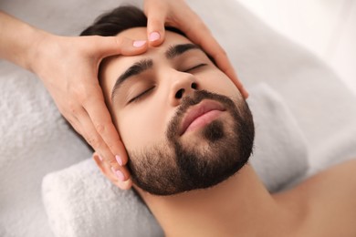 Photo of Young man receiving facial massage in beauty salon, closeup