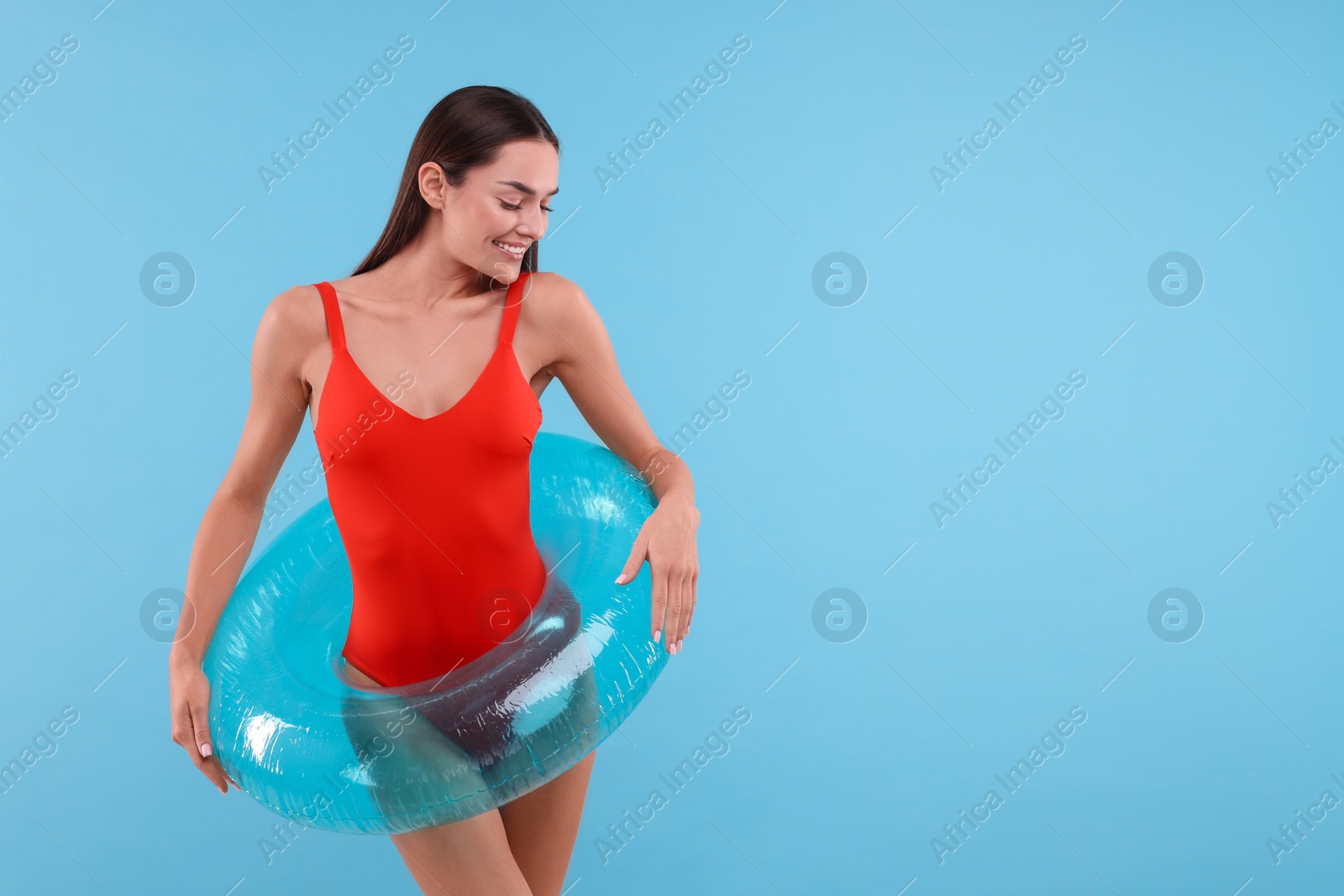 Photo of Young woman in stylish swimsuit with inflatable ring on light blue background, space for text