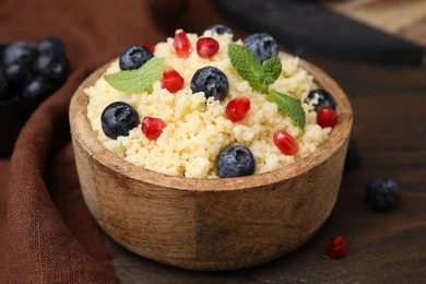 Photo of Bowl of tasty couscous with blueberries, pomegranate and mint on table, closeup