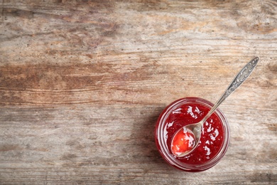 Photo of Jar and spoon with sweet jam on wooden background