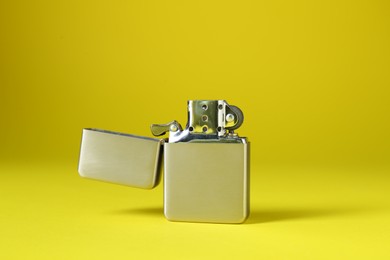 Photo of Gray metallic cigarette lighter on yellow background, closeup