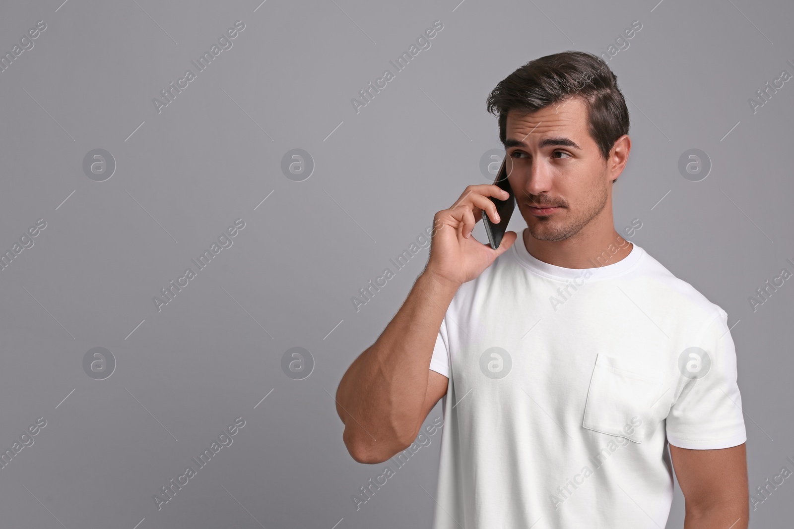 Photo of Handsome young man talking on smartphone against grey background. Space for text